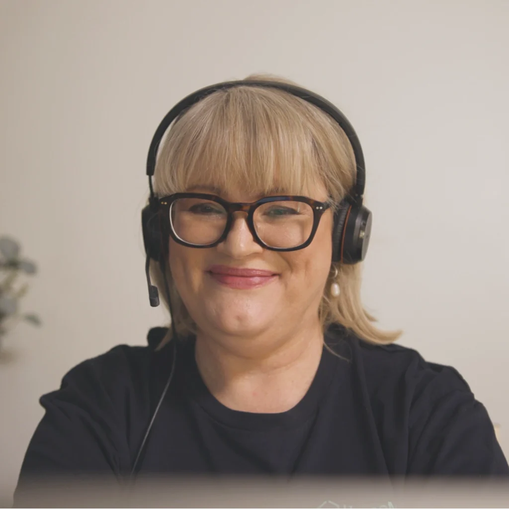 Person with blonde hair, black-framed glasses, and a headset, smiling at the camera.