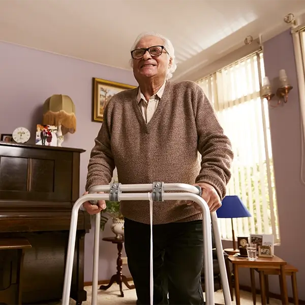 Elderly man smiling using his walking frame standing up in his living room.