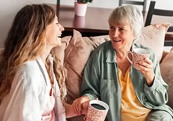 Two women sitting on a couch, smiling while holding mugs.