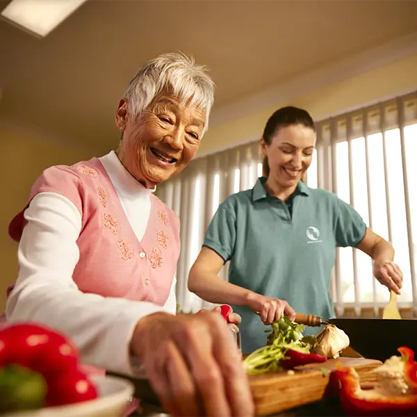 An older woman cooks with the help of her support worker.