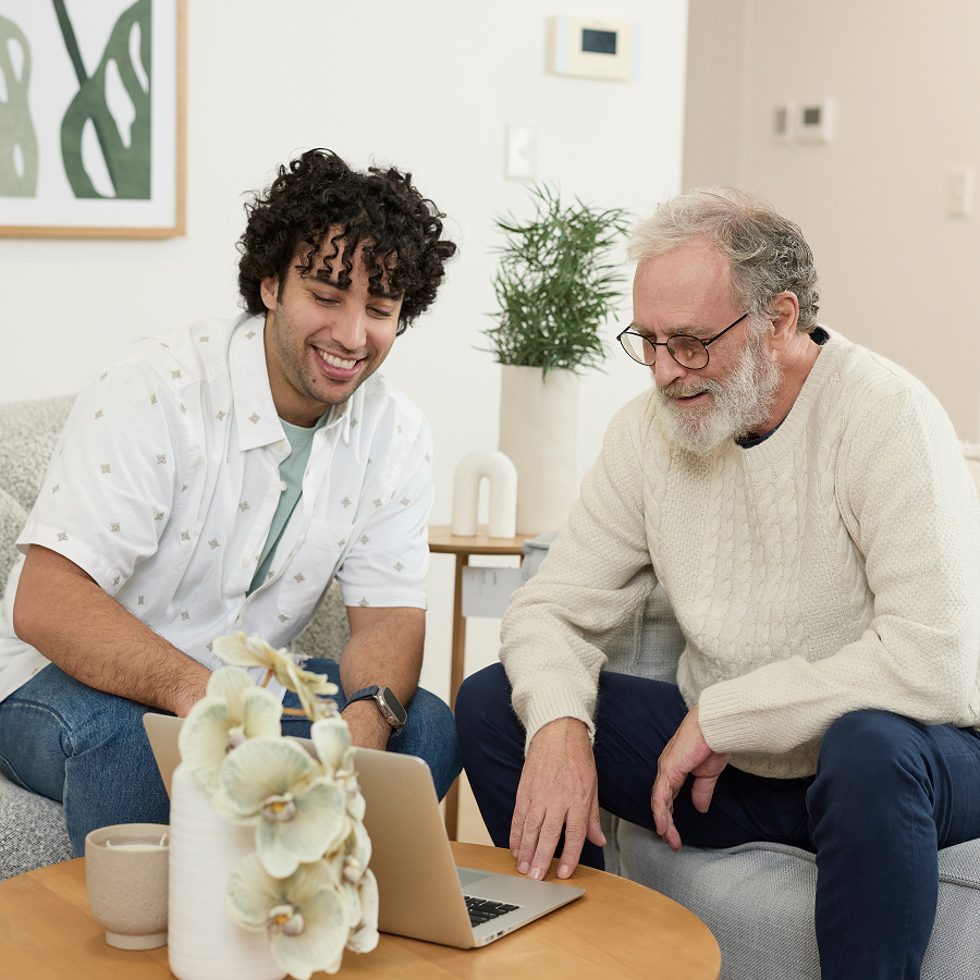 Support worker and elderly client looking at a laptop together at home.